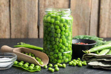 Fresh green peas in pickling jar, pods, spices and salt on black table, closeup
