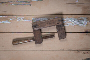 Old wooden clamp placed in the center on a rustic beige wooden table.
