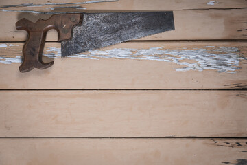 Old handsaw placed at the top left corner on a rustic beige wooden table. Space is left free for...