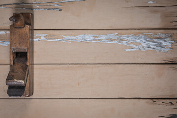 Old wooden hand plane placed on the left edge of a rustic beige wooden table. Space is left free...