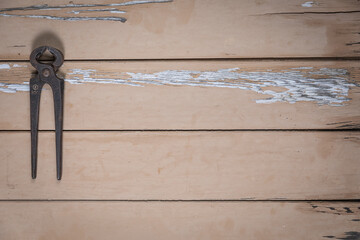 Old pincers placed on the left edge of a rustic beige wooden table. Space is left free for text or...