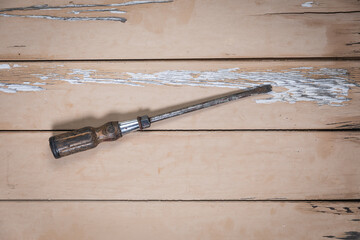 Large flathead screwdriver with wooden handle placed in the center on a rustic beige wooden table.
