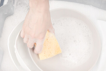 Female hand with sponge for washing dishes and bowls in water with foam or dishwashing liquid. washing dishes in the sink