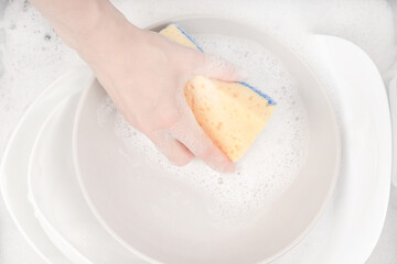 Female hand with sponge for washing dishes and bowls in water with foam or dishwashing liquid. washing dishes in the sink