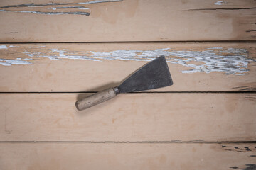 Old putty knife placed diagonally in the center on a rustic beige wooden table.
