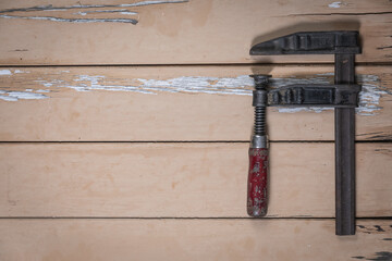 Old metal clamp with wooden handle placed on the right edge of a rustic beige wooden table. Space...