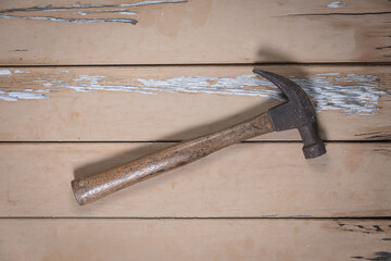 Old hammer with wooden handle placed diagonally in the center on a rustic beige wooden table.
