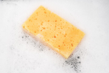 White pure foam with sponge for washing dishes. dishwashing foam and yellow sponge close up