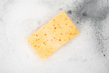 White pure foam with sponge for washing dishes. dishwashing foam and yellow sponge close up