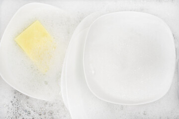 Yellow sponge for washing with dishes and bowls in water and foam or dishwashing liquid. washing dishes in the sink