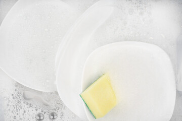 Yellow sponge for washing with dishes and bowls in water and foam or dishwashing liquid. washing dishes in the sink