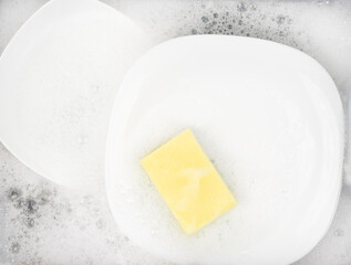 Yellow sponge for washing with dishes and bowls in water and foam or dishwashing liquid. washing dishes in the sink