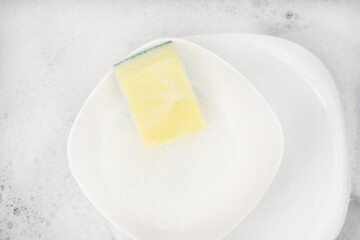 Yellow sponge for washing with dishes and bowls in water and foam or dishwashing liquid. washing dishes in the sink