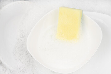 Yellow sponge for washing with dishes and bowls in water and foam or dishwashing liquid. washing dishes in the sink