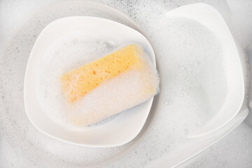 Yellow sponge for washing with dishes and bowls in water and foam or dishwashing liquid. washing dishes in the sink