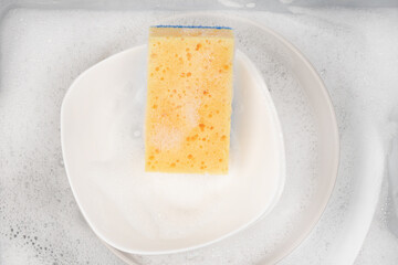 Yellow sponge for washing with dishes and bowls in water and foam or dishwashing liquid. washing dishes in the sink