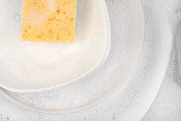 Yellow sponge for washing with dishes and bowls in water and foam or dishwashing liquid. washing dishes in the sink