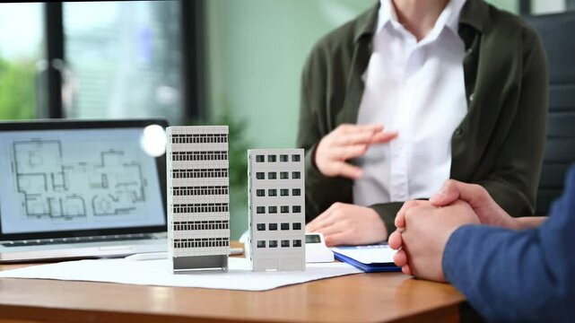 Real estate agent presenting floorplan to client with building models. Business consultation, investment planning