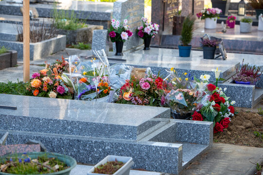 Une tombe fraiche dans un cimeti&egrave;re urbain. La s&eacute;pulture est recouverte de fleurs. La st&egrave;le et la pierre tombale ne sont pas encore en place. Sc&egrave;ne au soleil.