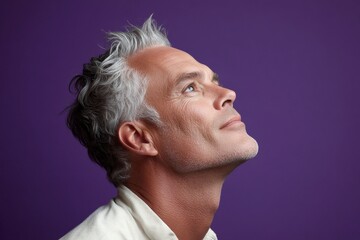 Fototapeta premium Purple solid background. A graceful mature man with a modern hairstyle. Concept art of style for aging men. Chic men's layered waves haircut - midlife white man with grey hair.
