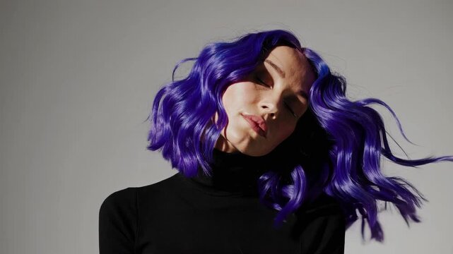 woman with blue hair, shoulder-length wavy style hair color is electric-purpel, solid background, hair roots slightly faded, black turtleneck sweater