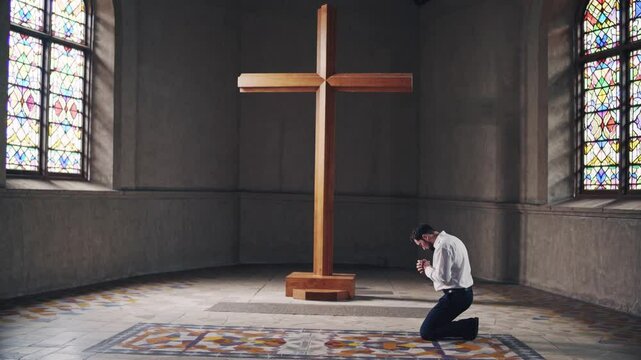 Man praying alone in a church interior with stained glass windows and large wooden cross, illustrating solitude in faith, religious commitment, forgiveness, spiritual sanctuary, and personal devotion