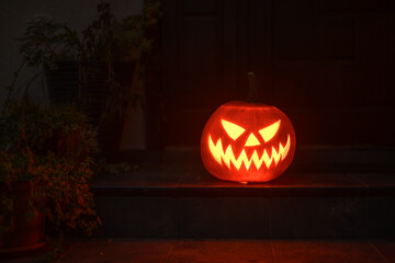Illuminated jack-o'-lantern glows warmly on on the steps in front of the house. Seasonal Halloween...
