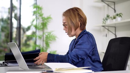 Experienced Asian senior woman collaborating on laptop and tablet in a modern professional office setting - Powered by Adobe