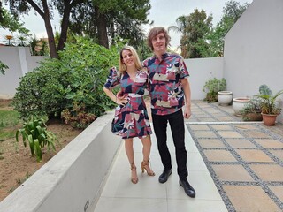 Man and a woman are standing in front of a white wall. The woman is wearing a dress and the man is...
