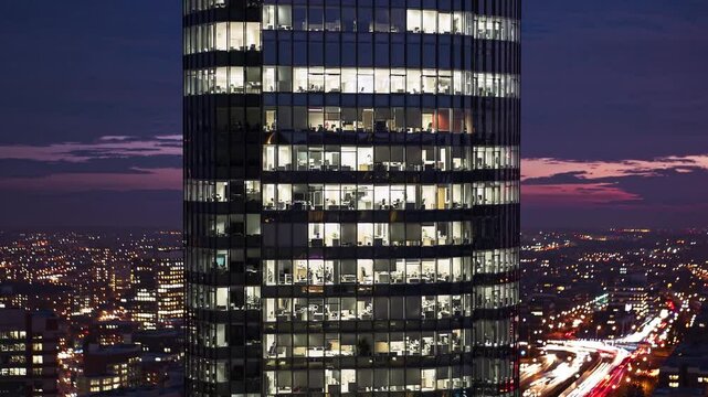 High-rise office tower glowing above city lights at sunset, representing economic growth, corporate influence, late-night productivity, ambition, and the symbolic power of illuminated success