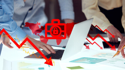 Business hands near laptop and financial reports, overlaid with red global map, padlock icon, and plunging stock chart. Concept of business urgency, stock market crash