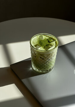 A glass of iced matcha latte placed on a closed laptop.