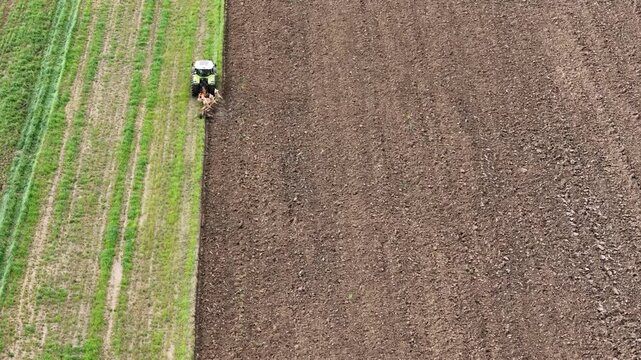 Aerial view of a farmer plowing the field with a tractor and preparing the land for sowing, creating a contrasting pattern of tilled soil and green vegetation in springtime, PC, Italy