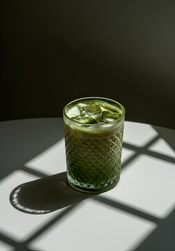 A single textured glass of iced matcha latte, partially framed on a clean light surface with a visible fold line. 