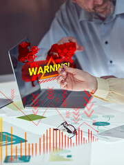 Laptop with digital red warning sign, world map, and security icons over hands and office docs...