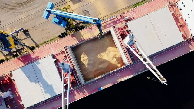 Dynamic drone descent as crane unloads grain into ship in Latvian port terminal