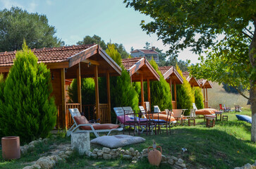 Obraz premium A small wooden house with a porch and a patio. The house has a wooden roof and a wooden door. The patio has a table and chairs, and a few lounge chairs. The lawn is green and well-maintained