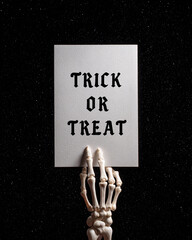 Skeleton hand holding a piece of paper with an inscription 'Trick or treat' against a dark starry sky background. Halloween decor concept. Fantasy illustration for poster, lettering, greeting card