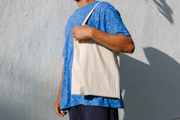 Man with black, tan skin holding in hand white eco cotton textile bag. Street urban wall...