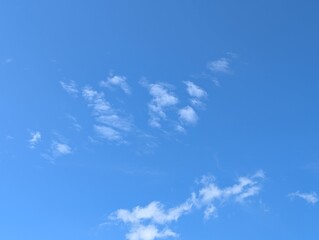 Clear blue sky with scattered white clouds on a sunny day, perfect for use as a background or...