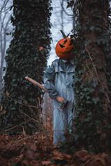 Creepy scarecrow with pumpkin head and axe weapon in hand inside autumn woods. Dark Halloween...