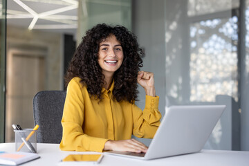 A businesswoman celebrates a victory while working on her laptop, radiating success and confidence....