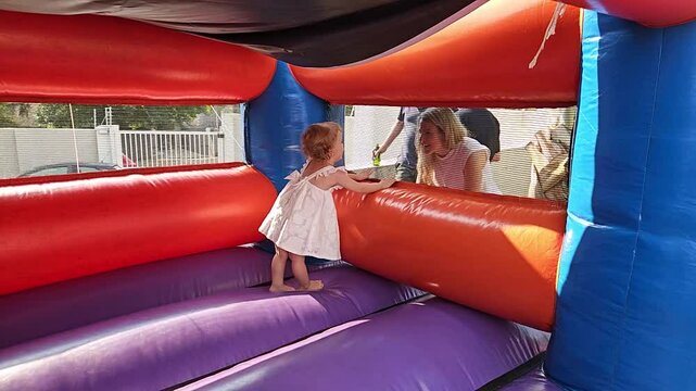 Woman is holding a child hand as they look out of a bounce house. The bounce house is red and blue in Johannesburg in South Africa