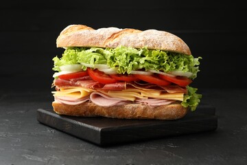 Tasty baguette sandwich with ham and vegetables on black table, closeup