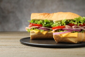 Pieces of tasty baguette sandwich with ham, cheese and vegetables on wooden table against grey background, closeup