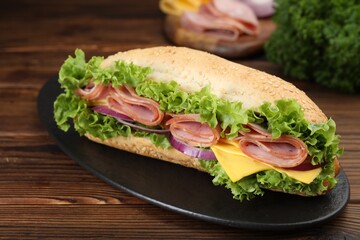 Tasty baguette sandwich with ham, cheese and vegetables on wooden table, closeup