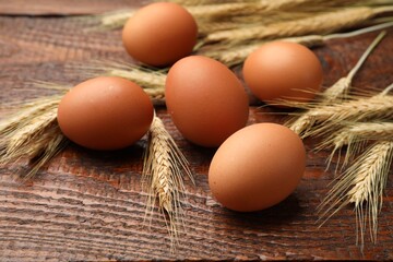 Raw eggs and spikes of wheat on wooden table, closeup