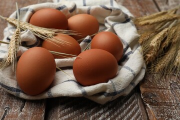Raw eggs, fabric and spikes of wheat on wooden table, closeup