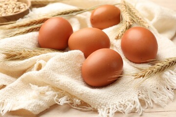 Fresh eggs, spikes and cloth on light wooden table, closeup