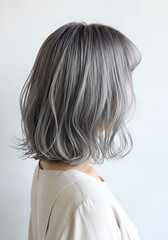 Fototapeta premium A young woman from directly behind. She has medium-length, slightly wavy, shiny grey hair and is wearing simple, elegant clothing. 